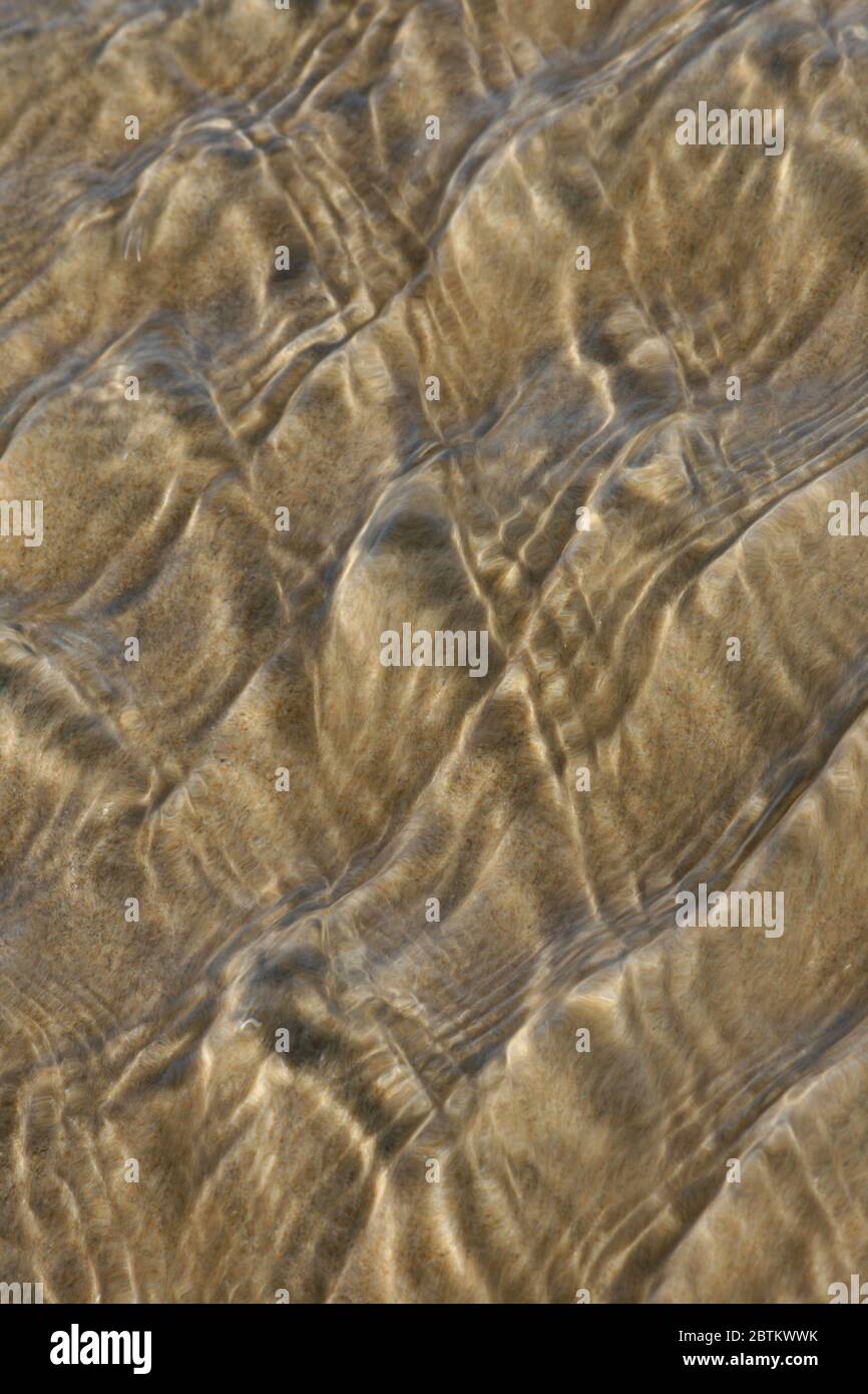 effetto astratto del movimento dell'acqua su un fondo sabbioso con riflessi soleggiati Foto Stock