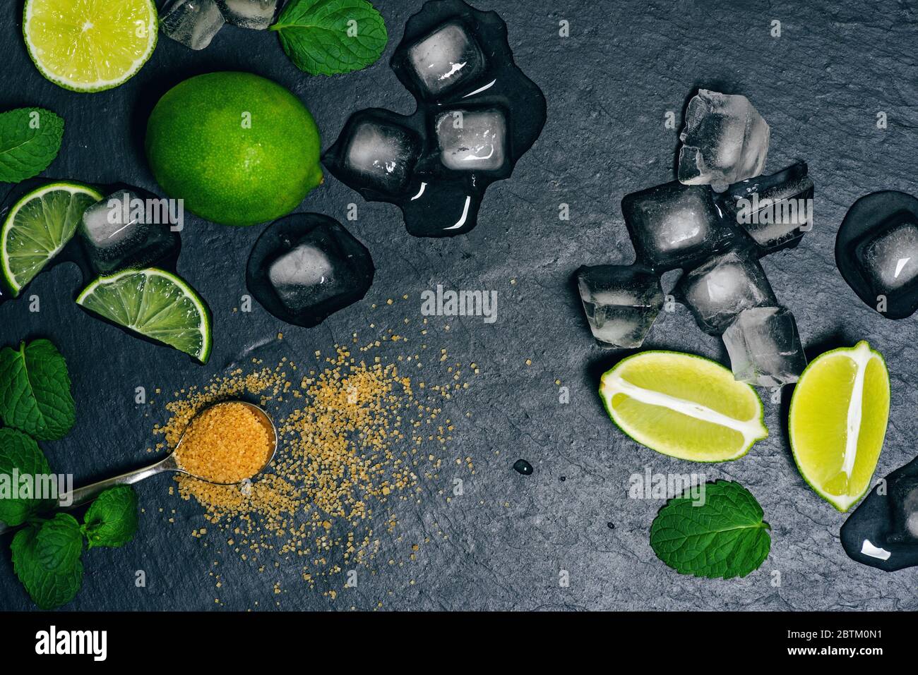 Vista dall'alto di menta fresca, lime, ghiaccio, zucchero su sfondo nero ingredienti per mojito. Foto Stock