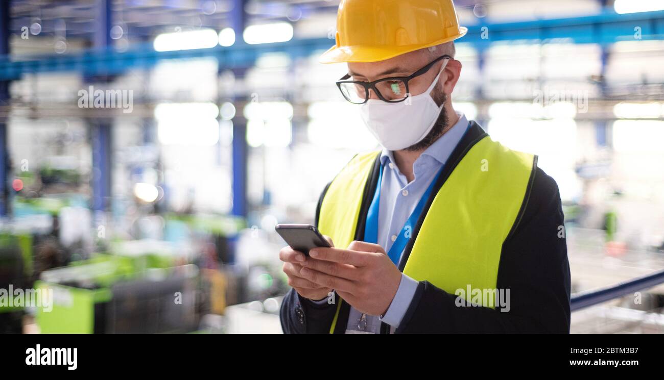 Tecnico o tecnico con maschera protettiva e telefono in fabbrica industriale. Foto Stock