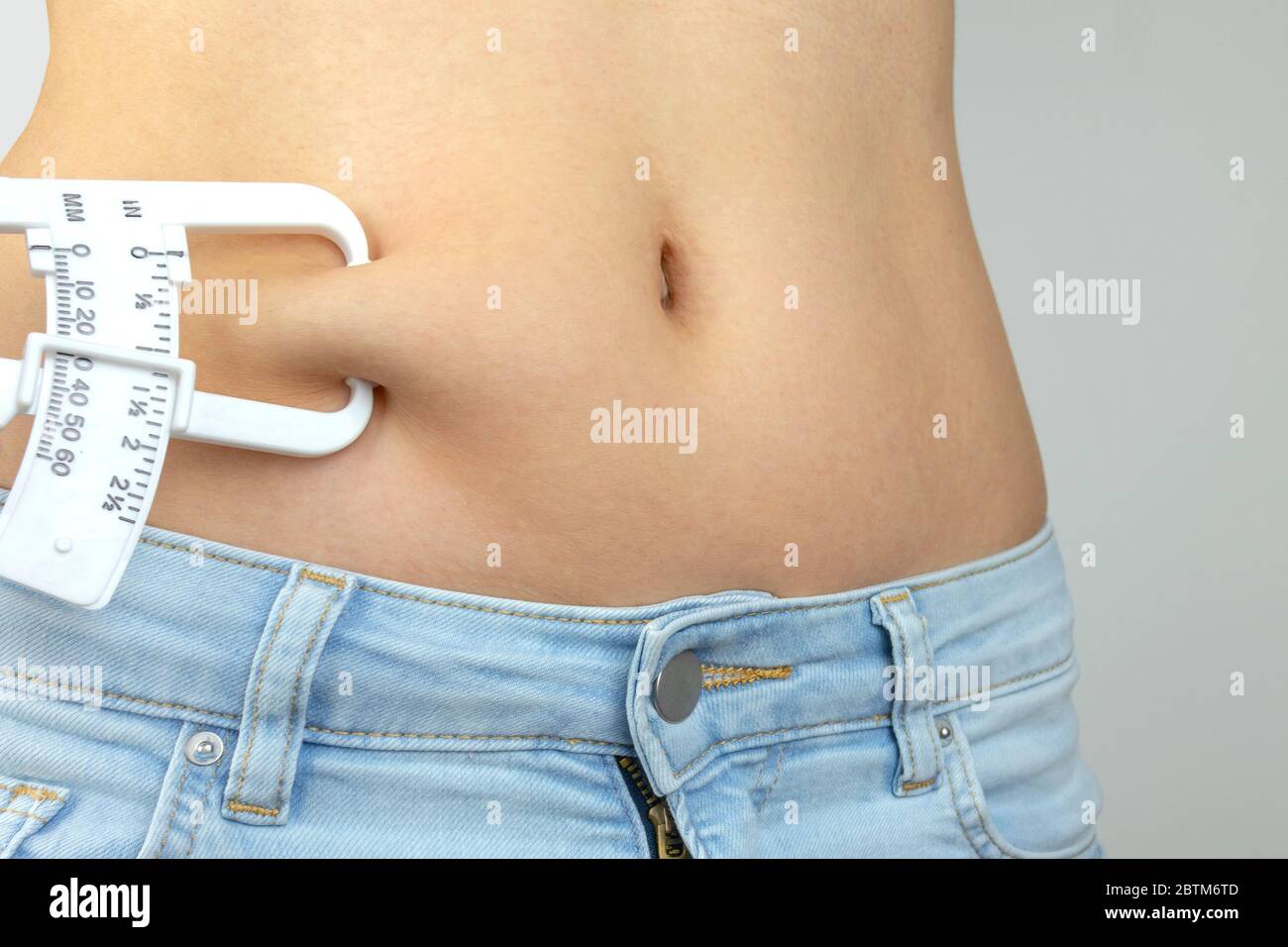 Calibri grassi del corpo, donna che misura la percentuale sottocutanea di grasso sulla pancia. Giovane donna che usa calibri a pieghe. Foto Stock