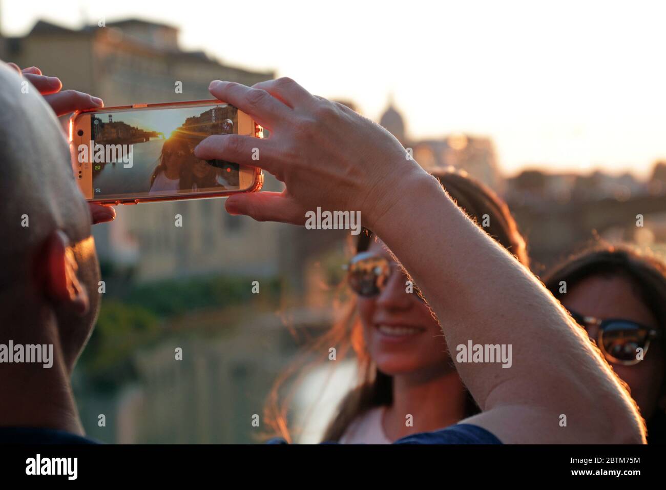 Firenze, Italia - 12 settembre 2019: Un uomo scatta una foto di due donne con il suo smartphone durante il tramonto sul famoso Ponte Vecchio di Firenze Foto Stock