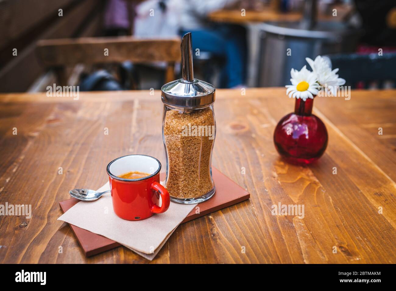 Tavolo da caffè all'aperto con un espresso in tazza sul tavolo e decorazione floreale sullo sfondo. Foto Stock