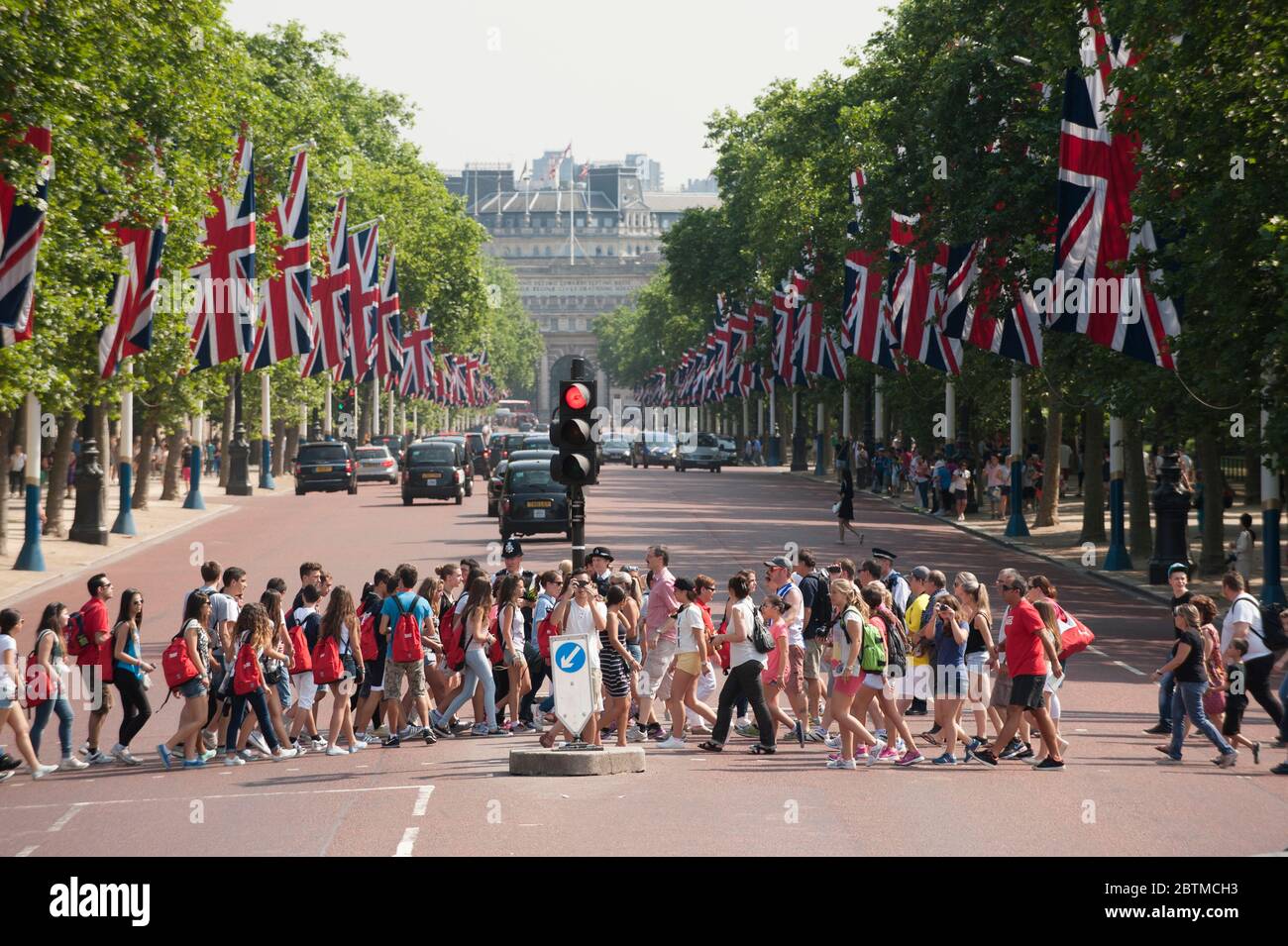 Grande groug di turisti che attraversano il Mall nel centro di Londra con bandiere Union che costeggiano la strada in un giorno d'estate Foto Stock