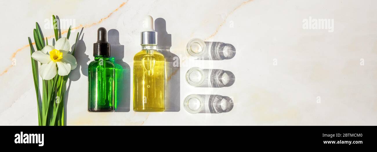 Olio omeopatico, siero e bottiglie con piante su sfondo marmoreo Banner Foto Stock