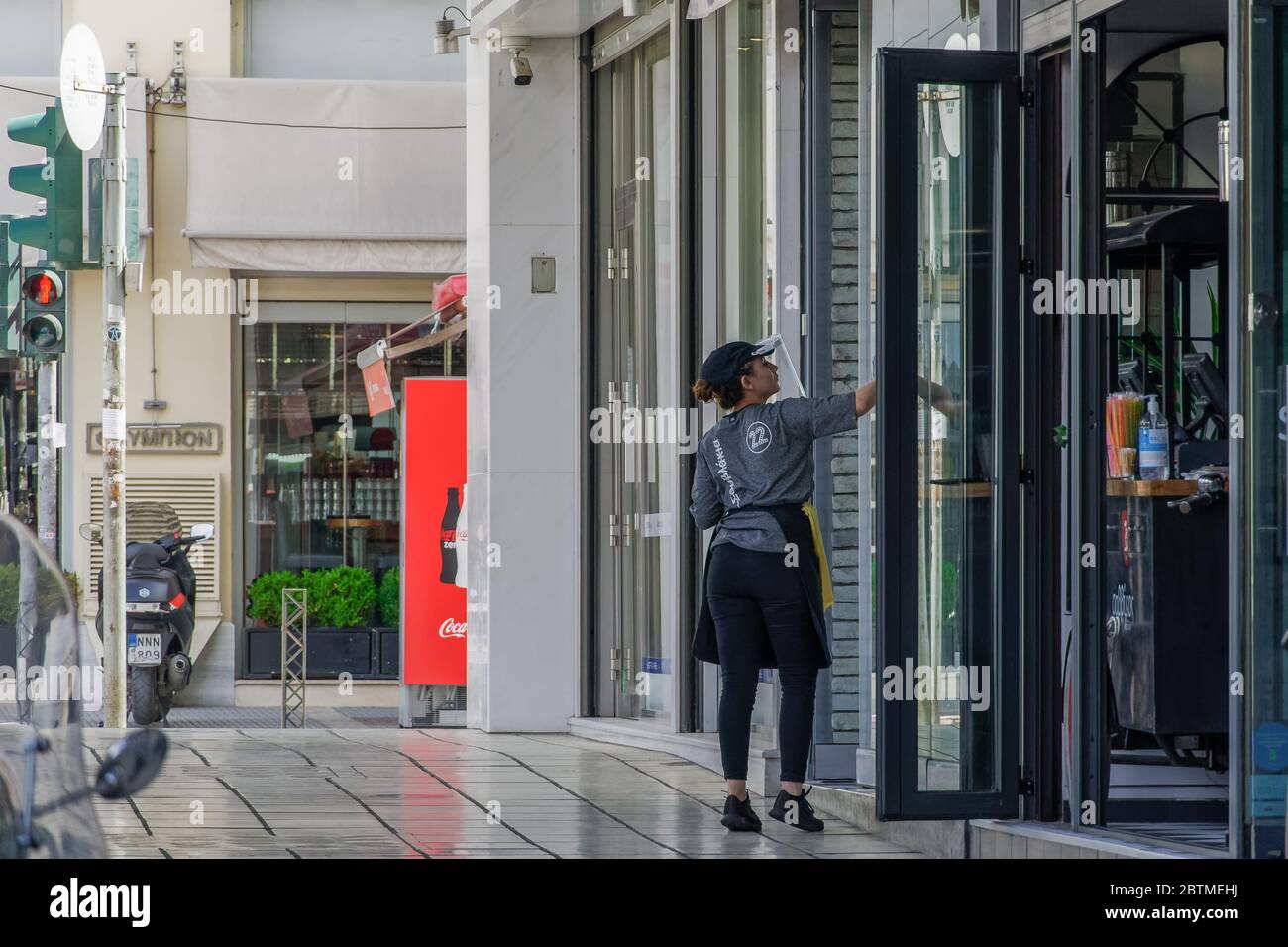 Salonicco, Grecia - Maggio 25 2020: Bar aperti per il primo giorno d'estate. L'impiegato con maschera protettiva pulisce l'ingresso del negozio di alimentari, dopo che il governo ellenico allenta le misure COVID-19 del coronavirus. Foto Stock