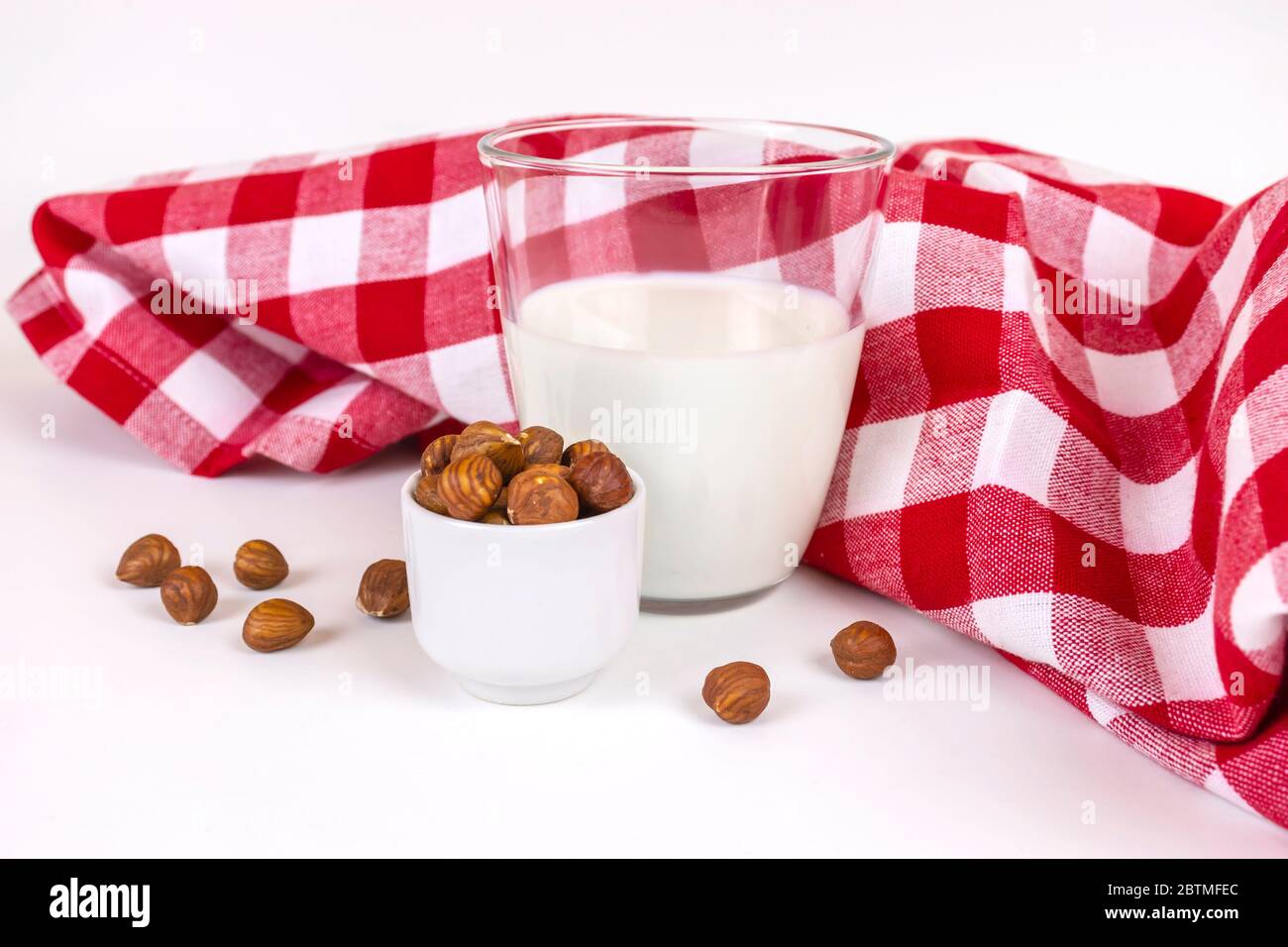 Bicchiere di latte fresco di nocciola vegana stile rustico. Un mucchio di nocciole in una tazza bianca e un bicchiere di latte fresco a base di noci bianche. Foto Stock