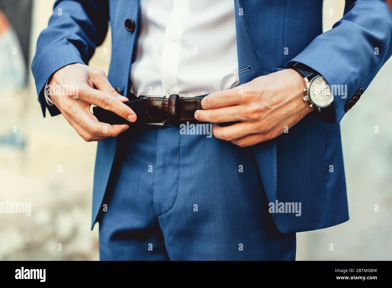 Sposo con pantaloni blu e una camicia bianca si allacciano alla cintura di  pelle. Grumi. Dettagli del matrimonio Foto stock - Alamy