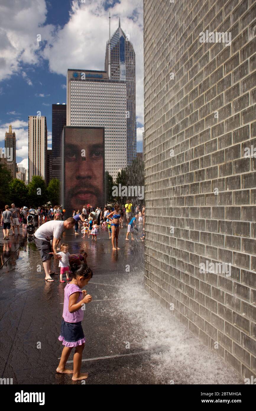 Foto verticale di un bambino che si rinfresca alla fontana della Jaume Plensa Crown con lo skyline di Chicago come sfondo, Millenium Park, Illinois, USA Foto Stock