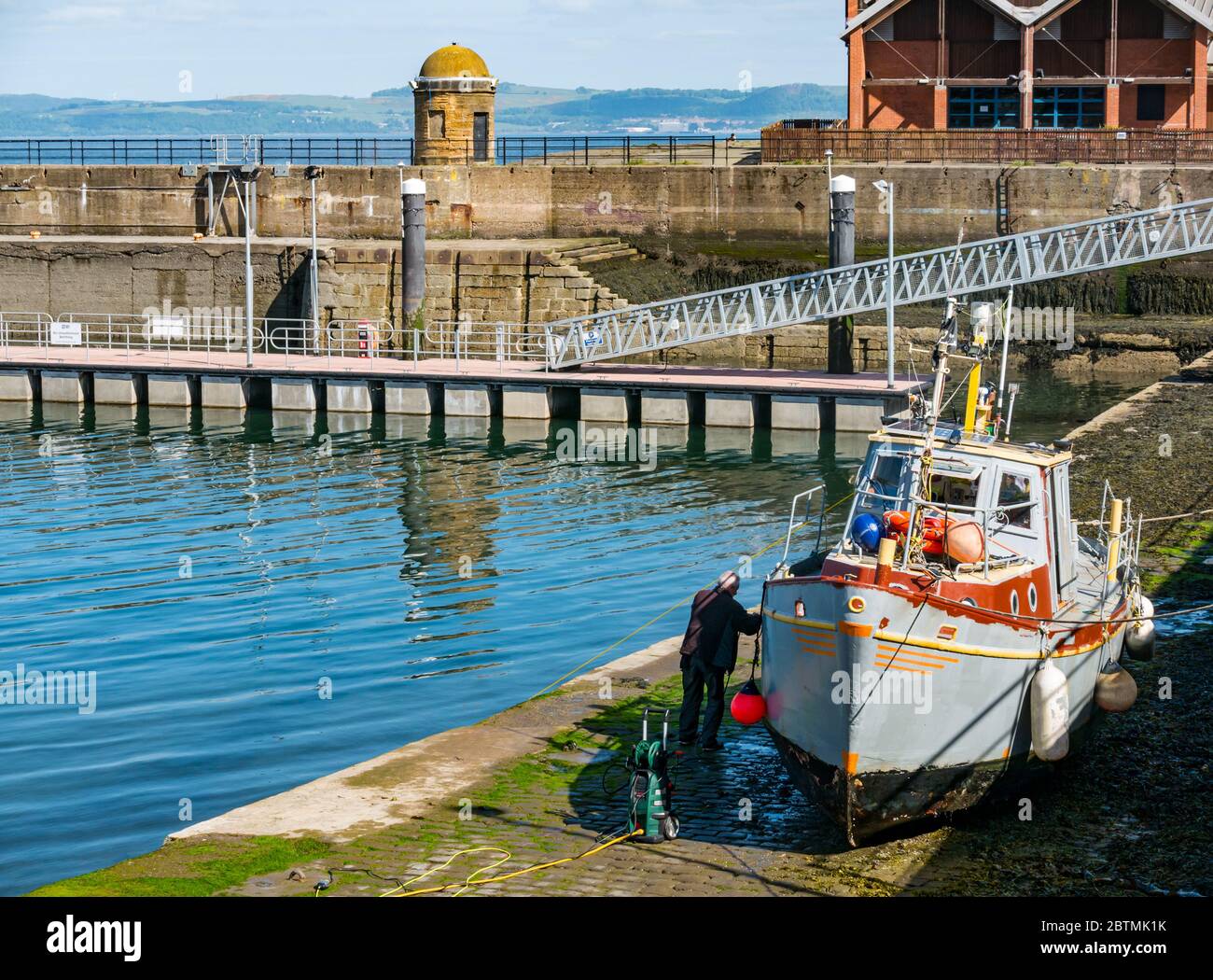 Newhaven, Edimburgo, Scozia, Regno Unito, 27 maggio 2020. UK Weather: Riflessioni in una calda giornata di sole con una barca da pesca che ottiene uno scafo pulito con un getto ad alta potenza spray Foto Stock