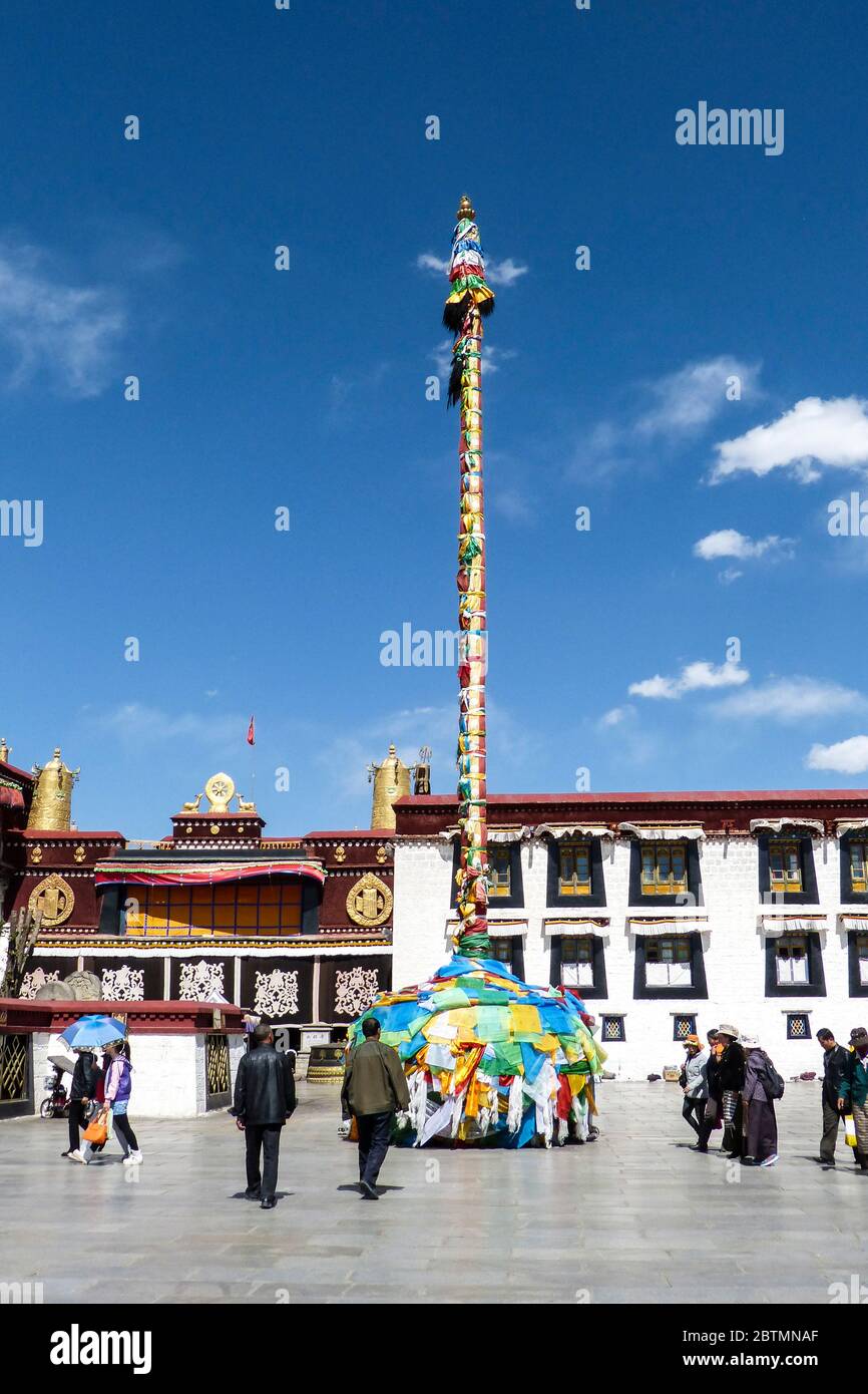 Uno dei grandi pali di preghiera che si ergono alti all'entrata del Tempio di Jokhang adornato con bandiere di preghiera contro il bel cielo azzurro e limpido Foto Stock