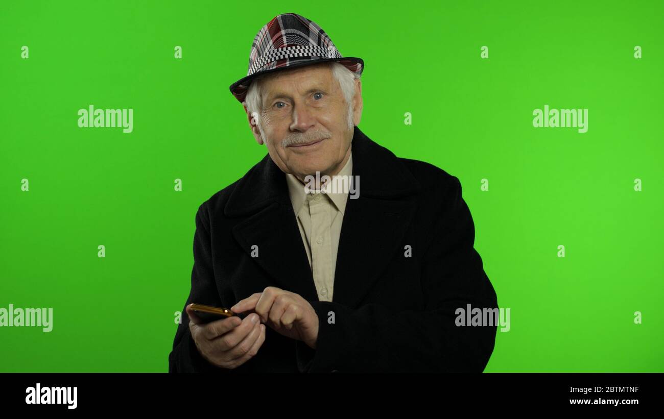 Anziano nonno alla moda uomo maturo caucasico che usa app sullo smartphone  per fare shopping online di successo. Sfondo chiave Chroma. Vecchio nonno  senior in moda vestiti di navigazione sul telefono cellulare