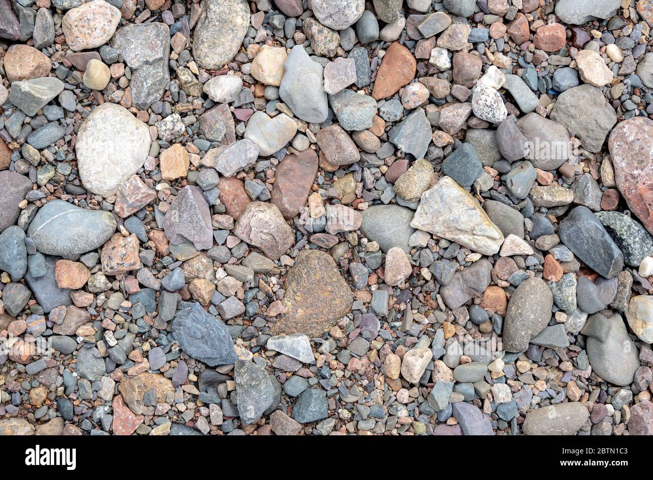 Un primo piano di una spiaggia rocciosa, guardando dritto verso il basso. Rocce di tutte le dimensioni e forme. Saturazione bassa. Foto Stock
