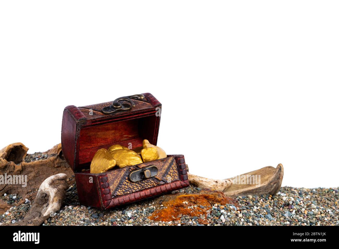 Un piccolo tesoro riempito di pepite d'oro. Chest è su una spiaggia sabbiosa con driftwood. Isolato su sfondo bianco adatto per testo o grafica. Foto Stock