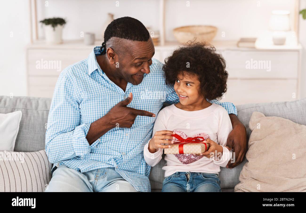 Festa di compleanno a casa. Il bambino afroamericano e il suo nonno scambiano regali di vacanza in soggiorno Foto Stock