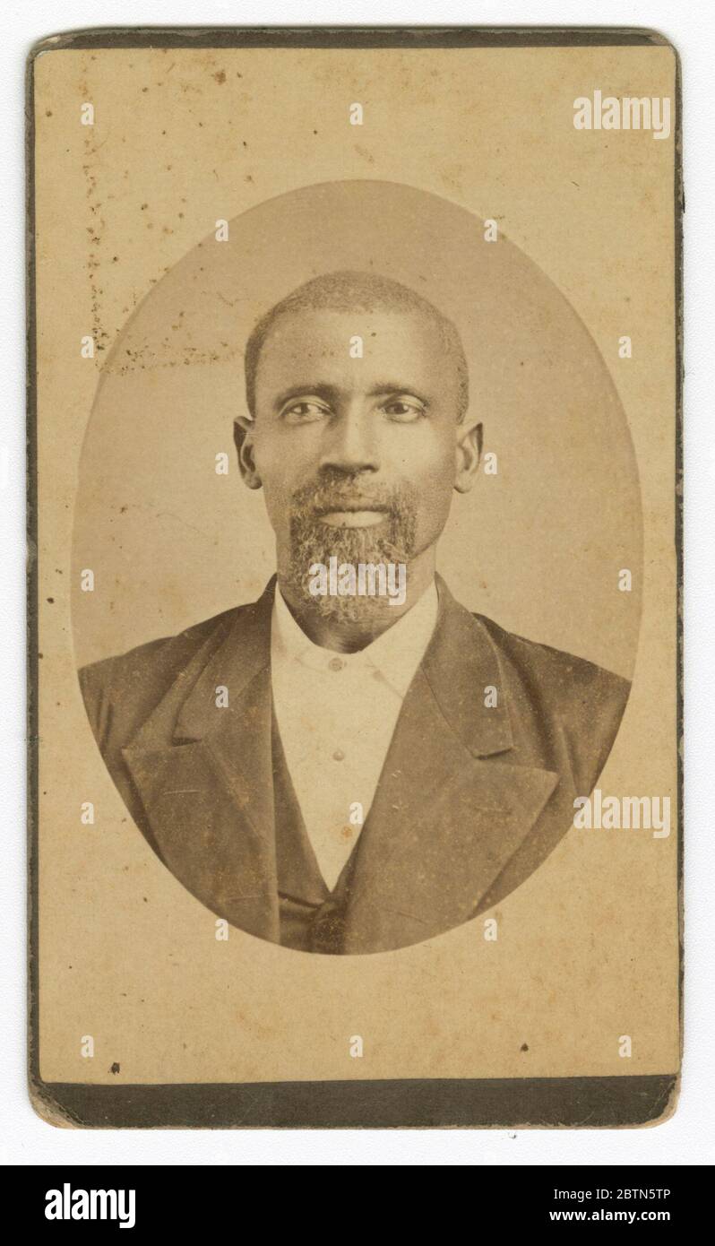 Fotografia di un uomo con barba e giubbotto di colore scuro. Un ritratto di uomo con barba dalle tonalità seppia. L'uomo indossa una giacca e un gilet di colore scuro e una camicia bianca. Sta guardando direttamente la fotocamera. L'immagine ha una forma ovale. Parte di un registro stampato è visibile sul retro. Foto Stock