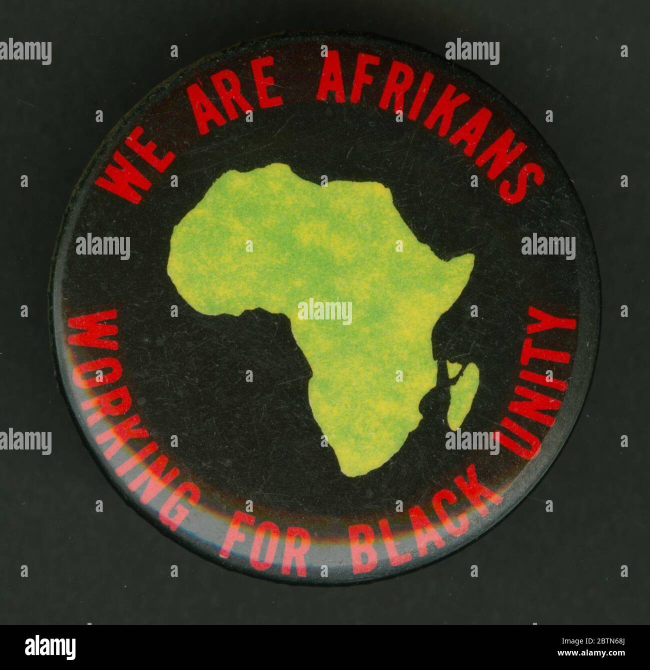 Pulsante Pinback che promuove l'unità nera. Pulsante rotondo con pin-back che mostra l'immagine verde centrale del continente africano. Il tipo rosso circoli l'Africa e legge [SIAMO AFRIKANS/LAVORANDO PER L'UNITÀ NERA]. Foto Stock