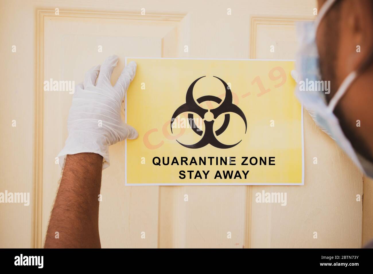 Il lavoratore di prima linea che applica il banner di Covid-19 o zona di quarantena del coronavirus rimanere lontano davanti alla porta in ospedale come nota di attenzione. Foto Stock