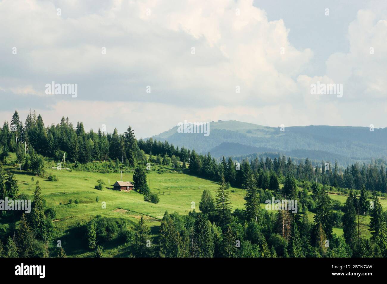 vecchia casa di legno e alberi in cima alle montagne di collina in estate soleggiata sullo sfondo di cielo e nuvole Foto Stock