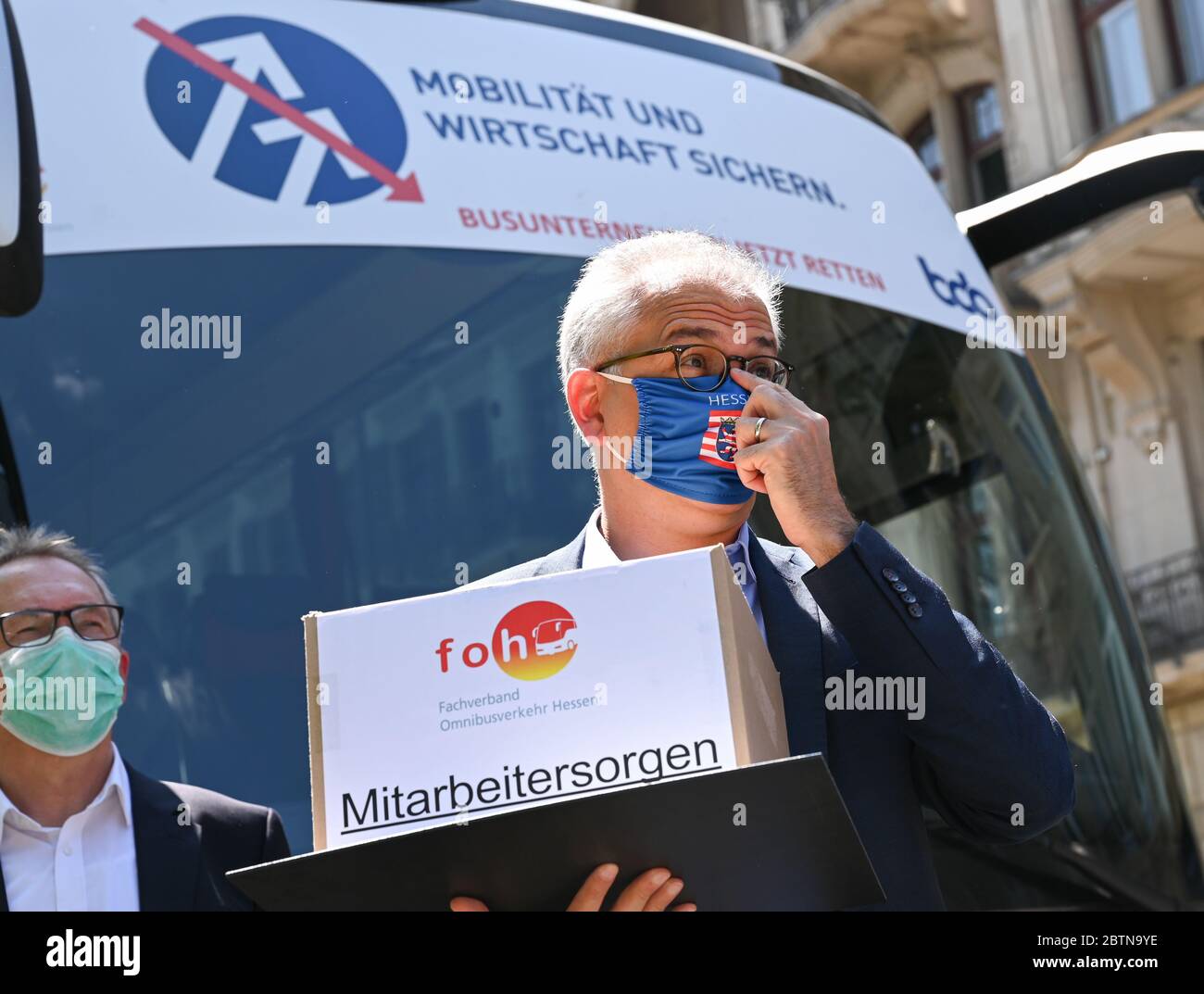 Wiesbaden, Germania. 27 maggio 2020. Tarek al-Wazir (Bündnis 90/Die Grünen), Ministro dell'Economia dello Stato dell'Assia, si trova di fronte ad un allenatore con l'iscrizione 'Sichern Mobilität und Witschaft sichern. Le compagnie di autobus ora salvano'. Le compagnie di autobus chiedono aiuti immediati a causa della crisi di Corona. Circa 100 autobus da tutta l'Assia hanno partecipato all'evento. Credit: Arne Dedert/dpa/Alamy Live News Foto Stock