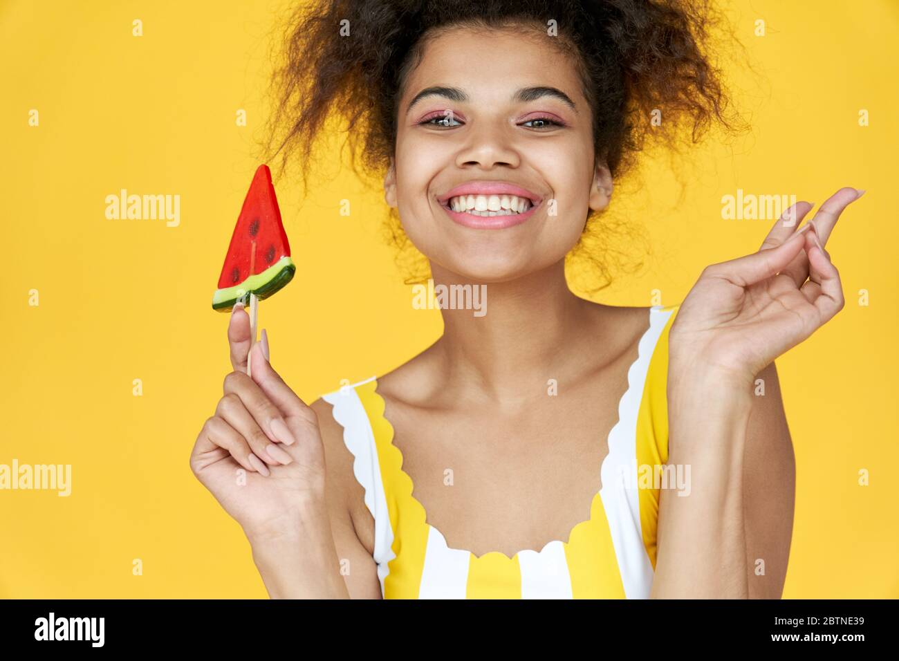 Felice africano gen z teen ragazza tenere caramella isolato su sfondo giallo estate. Foto Stock