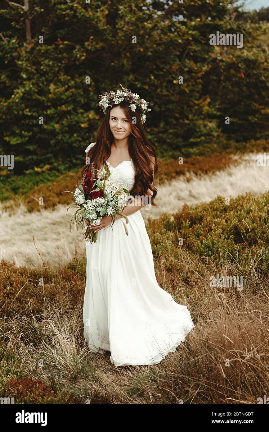 elegante sposa in posa con bouquet sullo sfondo della foresta, lussuoso boho matrimonio in montagna Foto Stock
