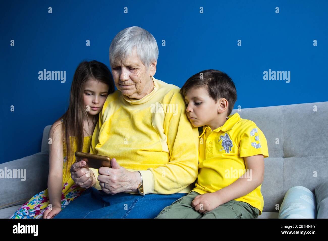 Una vecchia nonna e i suoi amati nipoti si siedono a casa e scattano foto sul loro smartphone Foto Stock