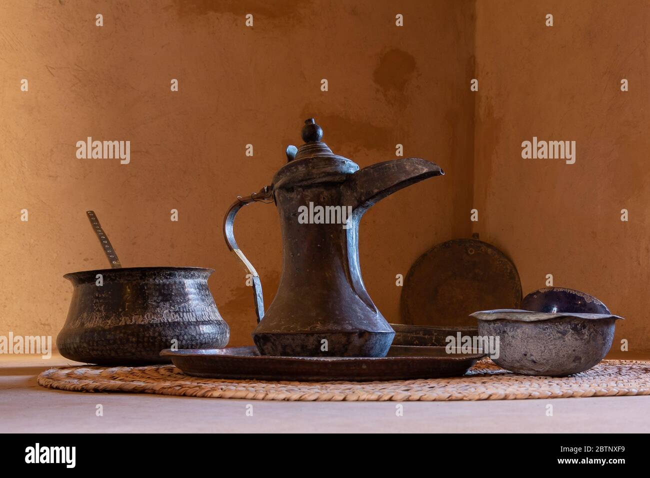 Caffettiera in stile Omani chiamata dallah e ciotole di fronte al muro di argilla marrone, Nizwa Foto Stock