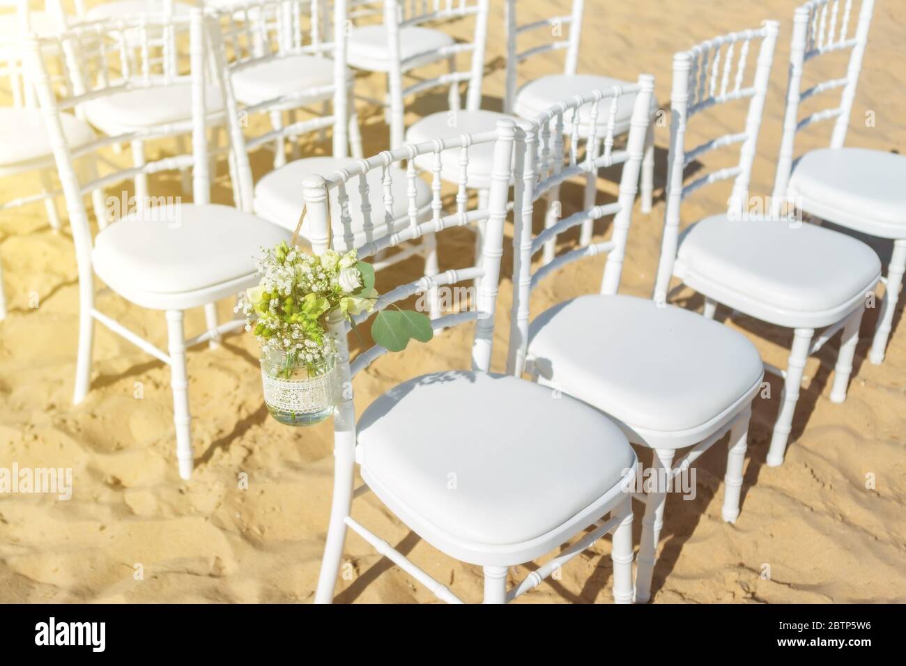 Cerimonia nuziale sulla spiaggia in una giornata di sole. Un set di sedie bianche per gli ospiti decorate con fiori. Foto Stock