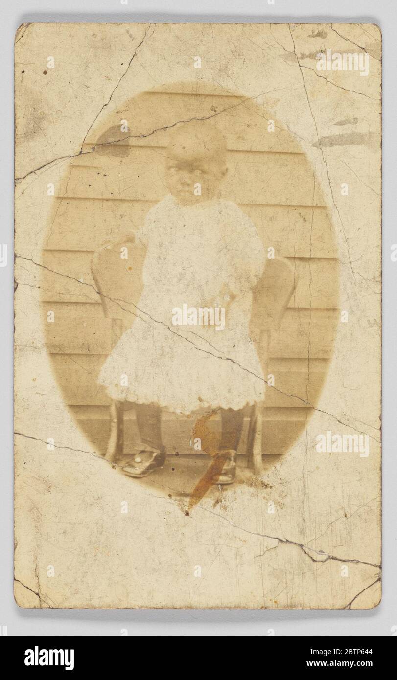 Cartolina fotografica di bambino non identificato. Una stampa fotografica di un bambino non identificato. Il bambino è raffiguro in un'immagine di forma ovale sulla parte anteriore della cartolina. Il bambino è posto in piedi sulla parte superiore di una sedia che indossa un abito di colore chiaro e calze e scarpe scure. Foto Stock