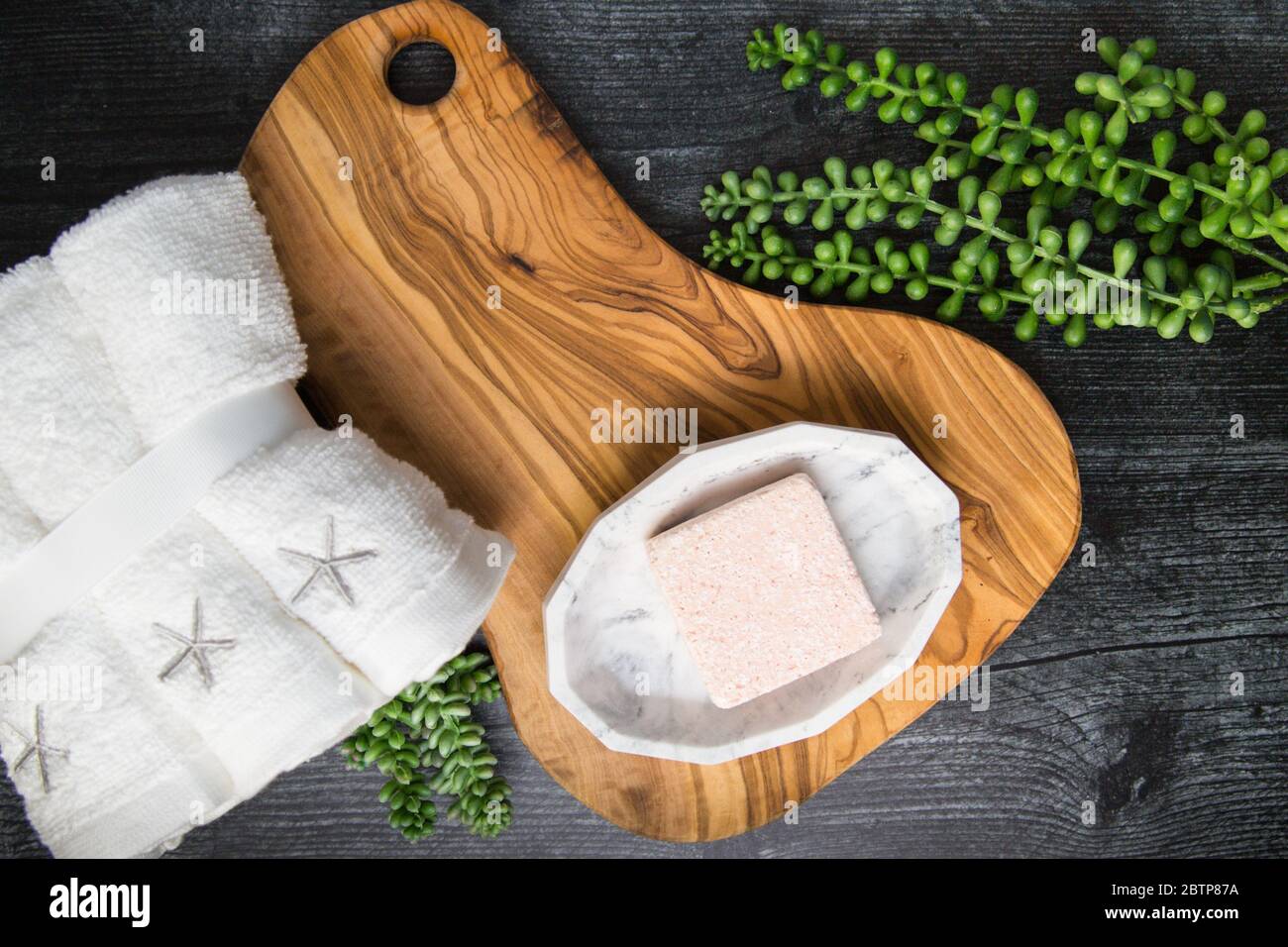 Piatto di bagno schiuma rosa cubo bomba su vassoio di legno con asciugamani e succulenti pronti per essere utilizzati per un rilassante esperienza spa Foto Stock