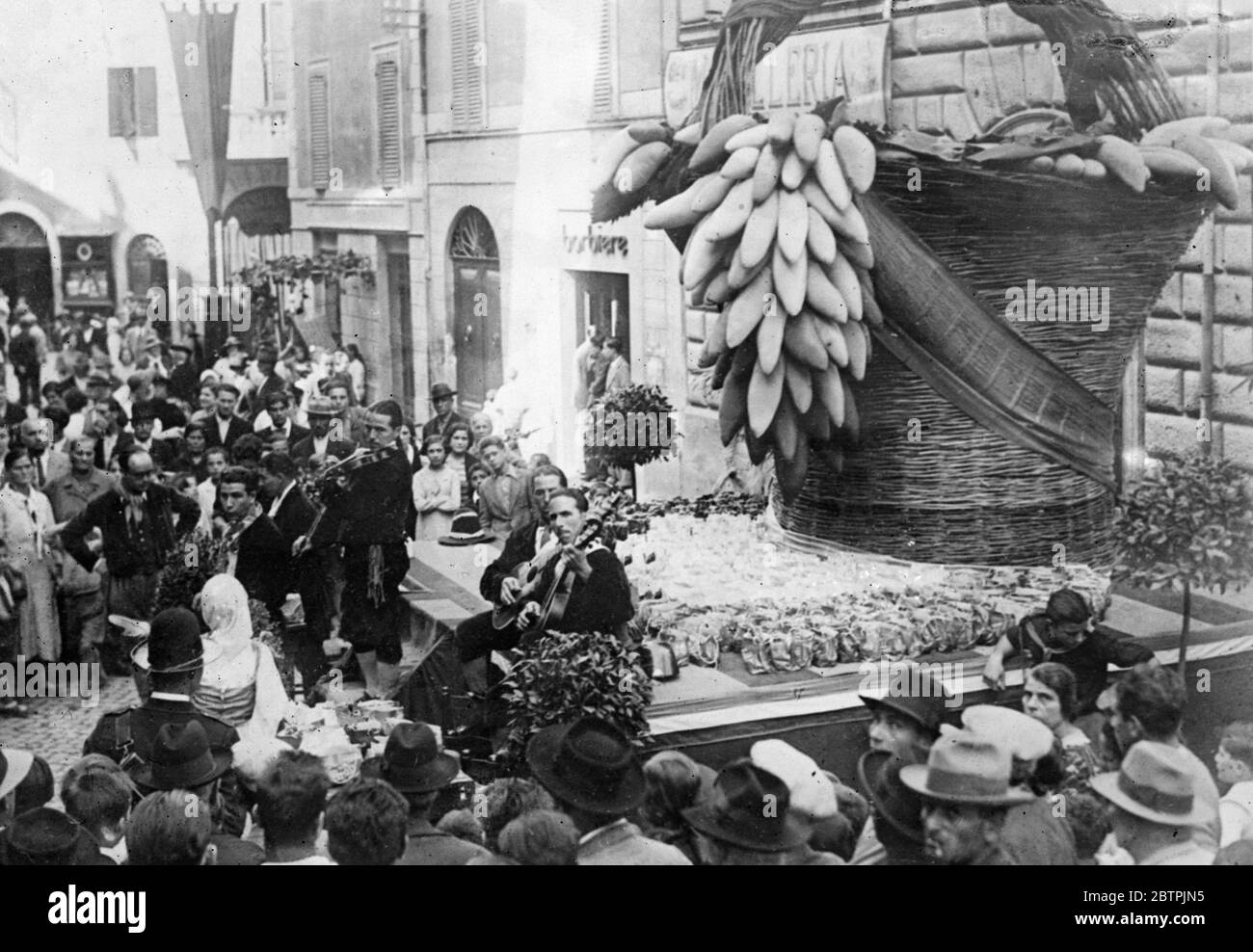 Festa dell'uva a Tivoli . La tradizionale Festa dell'uva è stata celebrata a Tivoli , in Italia . Foto mostra musicisti che suonano a una folla in una strada a Tivoli durante il festival di fronte a una mostra di un gigantesco cesto di uve. Settembre 1934 Foto Stock