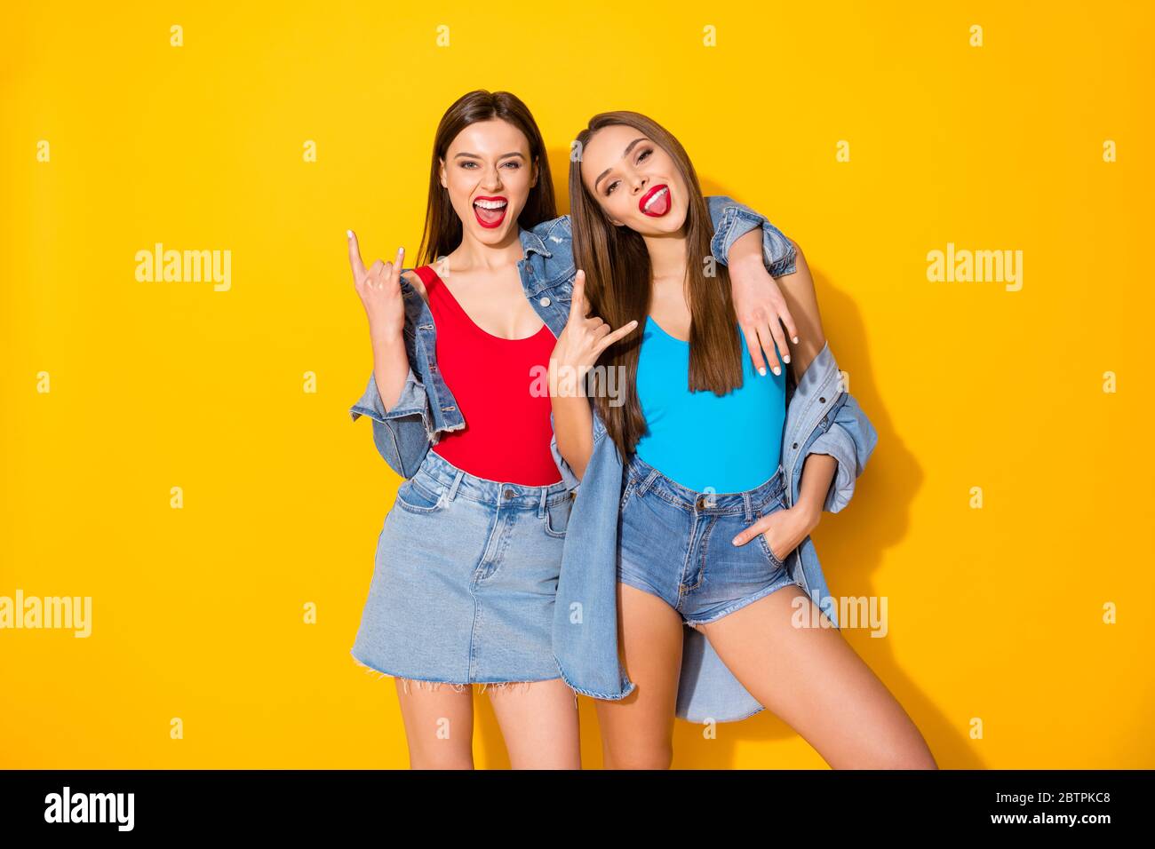 Ritratto di ragazze divertenti ed eccitate pazzesche godono di rock e roll pank fine settimana spettacolo corna simbolo indossare jeans canotta isolato sopra luminoso colore Foto Stock
