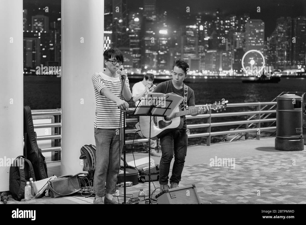 Hong Kong / Cina - 25 luglio 2015: Giovani musicisti di strada che si esibiscono nella passeggiata di Tsim Sha Tsui di Kowloon, con vista sui grattacieli di Hong Kong Isla Foto Stock