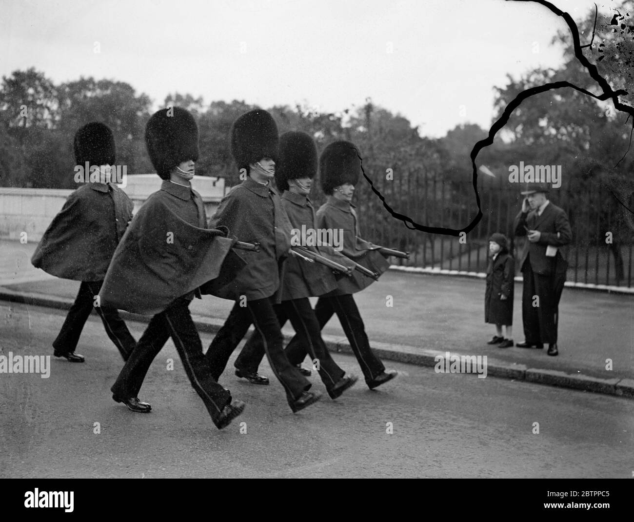 Tenendo le loro braccia asciutte. Le guardie indossano i loro cappe, un segnale sicuro che il tempo è 'nessuno a buon' a Londra quando hanno marciato attraverso St JaME's Park sulla loro strada per Wellington Barracks oggi (Domenica). 10 luglio 1938 Foto Stock
