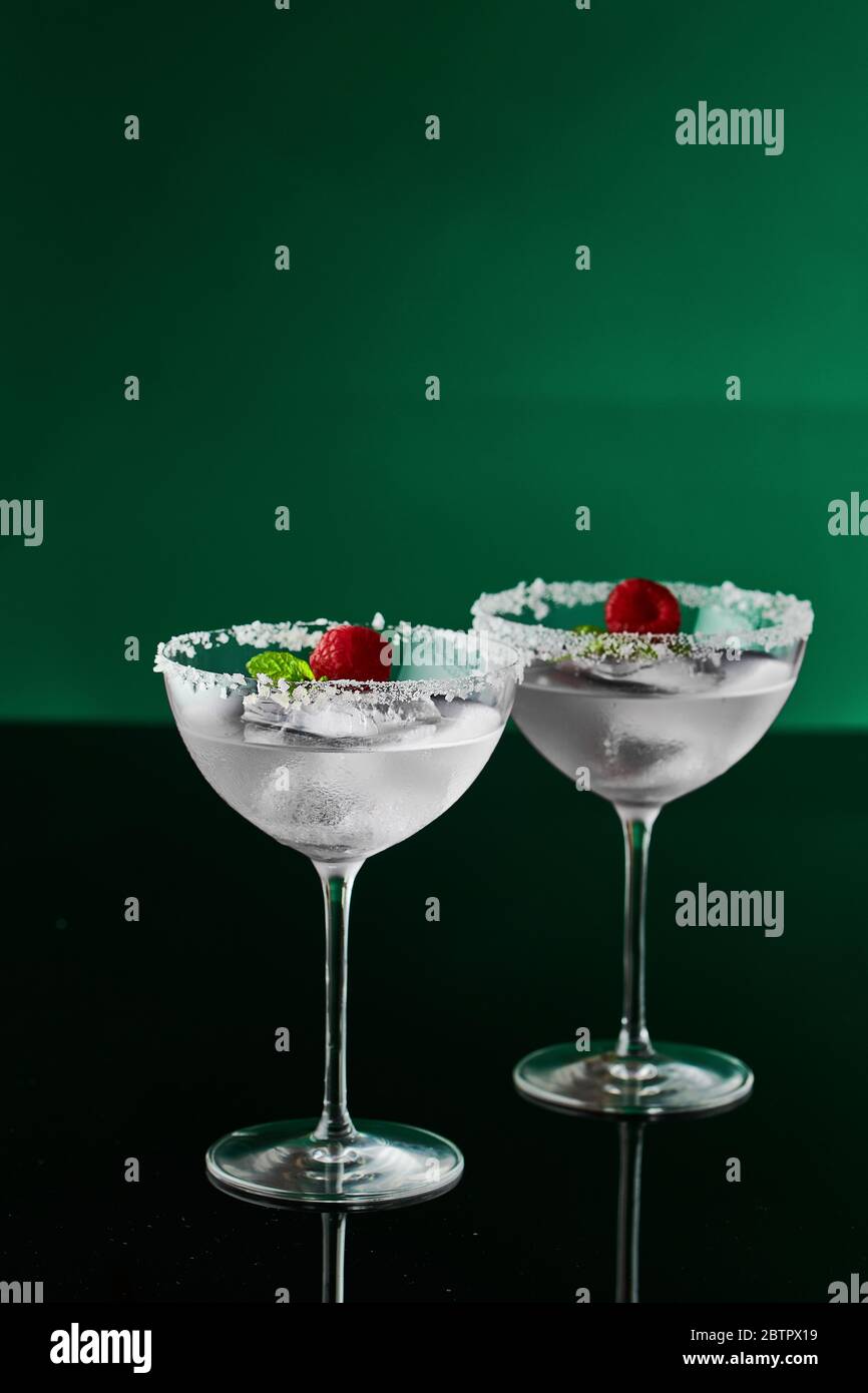 Bicchieri da cocktail con gin rosa e tonico guarniti con un grande pezzo di  ghiaccio, menta piperita e lampone con cristalli di sale sul bordo del  bicchiere Foto stock - Alamy