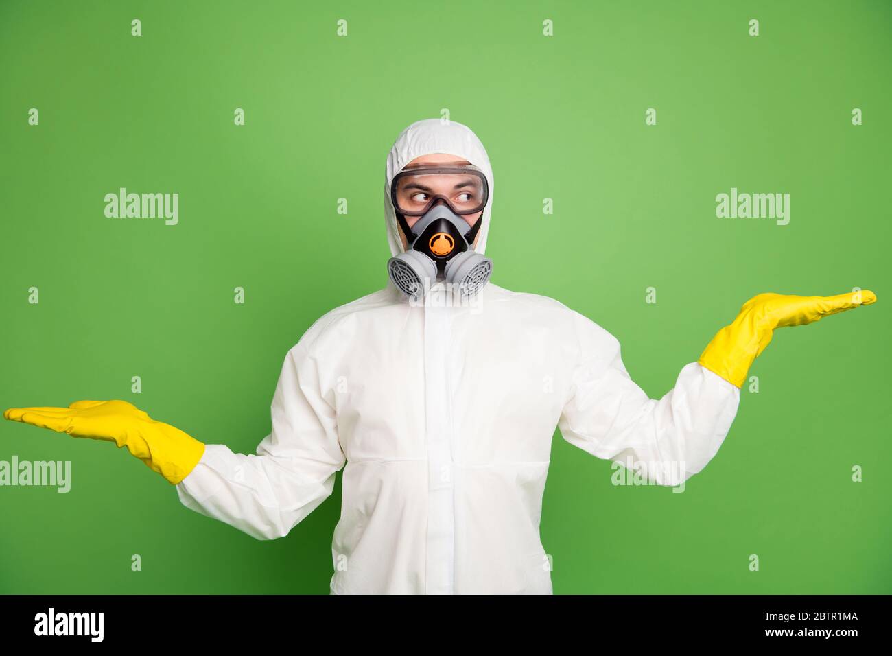 Ritratto di uomo incerto tenere mano guardare copyspace dimostrare ncov annunci promozione indossare bianco lattice Hazmat uniforme isolato su sfondo di colore verde Foto Stock
