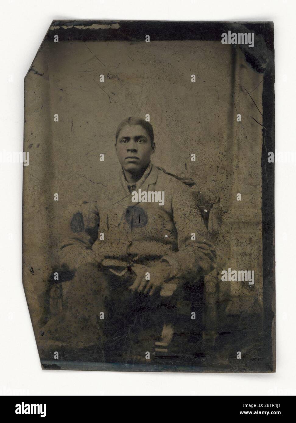 Tintype di un uomo. Un tipo di uomo afro-americano non identificato seduto con gambe incrociate. Indossa un cappotto e pantaloni, e le sue guance sono state dipinte di rosa. Foto Stock Tintype di un uomo. Un tipo di uomo afro-americano non identificato seduto con gambe incrociate. Indossa un cappotto e pantaloni, e le sue guance sono state dipinte di rosa. Foto Stock