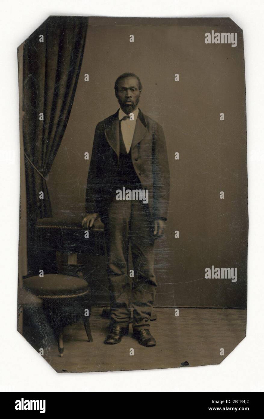 Tintype di un uomo. Una tinta di un uomo afro-americano non identificato in piedi per il suo ritratto davanti ad un drappeggio. Indossa una giacca, un gilet e una cravatta, e un anello d'oro è stato dipinto sul dito dell'anello destro. Foto Stock