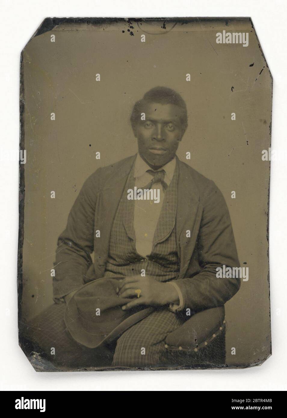 Tintype di un uomo. Una tintype di un uomo afro-americano non identificato seduto con il suo cappello in grembo. Indossa una cravatta, un gilet e una giacca, e un anello d'oro dipinto sul dito dell'anello sinistro. Foto Stock