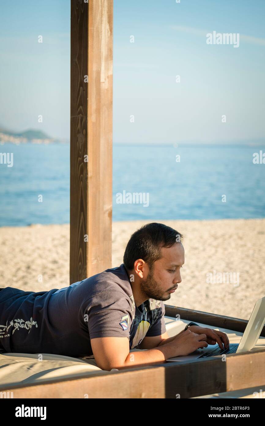 Un maschio che usa un computer portatile all'aperto in spiaggia Foto Stock