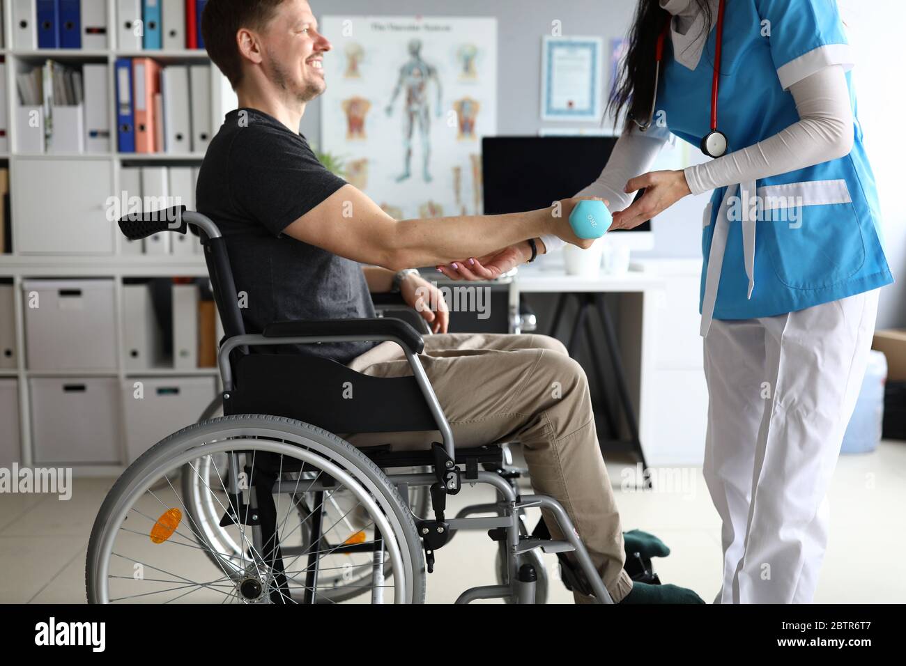 Il medico aiuta l'uomo su sedia a rotelle a tenere il manubro Foto Stock