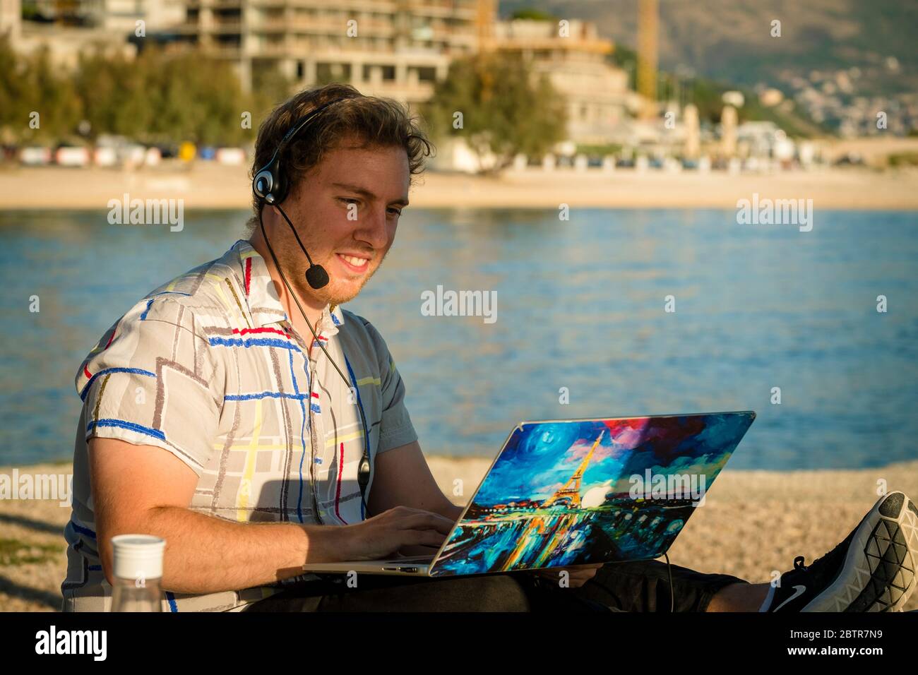 Un uomo che usa il laptop e le cuffie all'aperto in spiaggia Foto Stock
