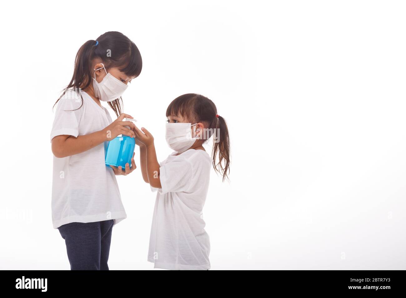 Due bambine indossano il facemask durante il coronavirus e l'epidemia di influenza. Protezione contro virus e malattie, igienizzante per le mani su sfondo bianco Foto Stock