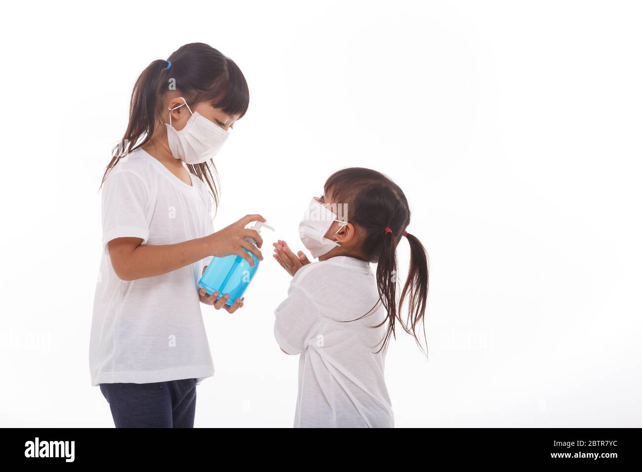 Due bambine indossano il facemask durante il coronavirus e l'epidemia di influenza. Protezione contro virus e malattie, igienizzante per le mani su sfondo bianco Foto Stock