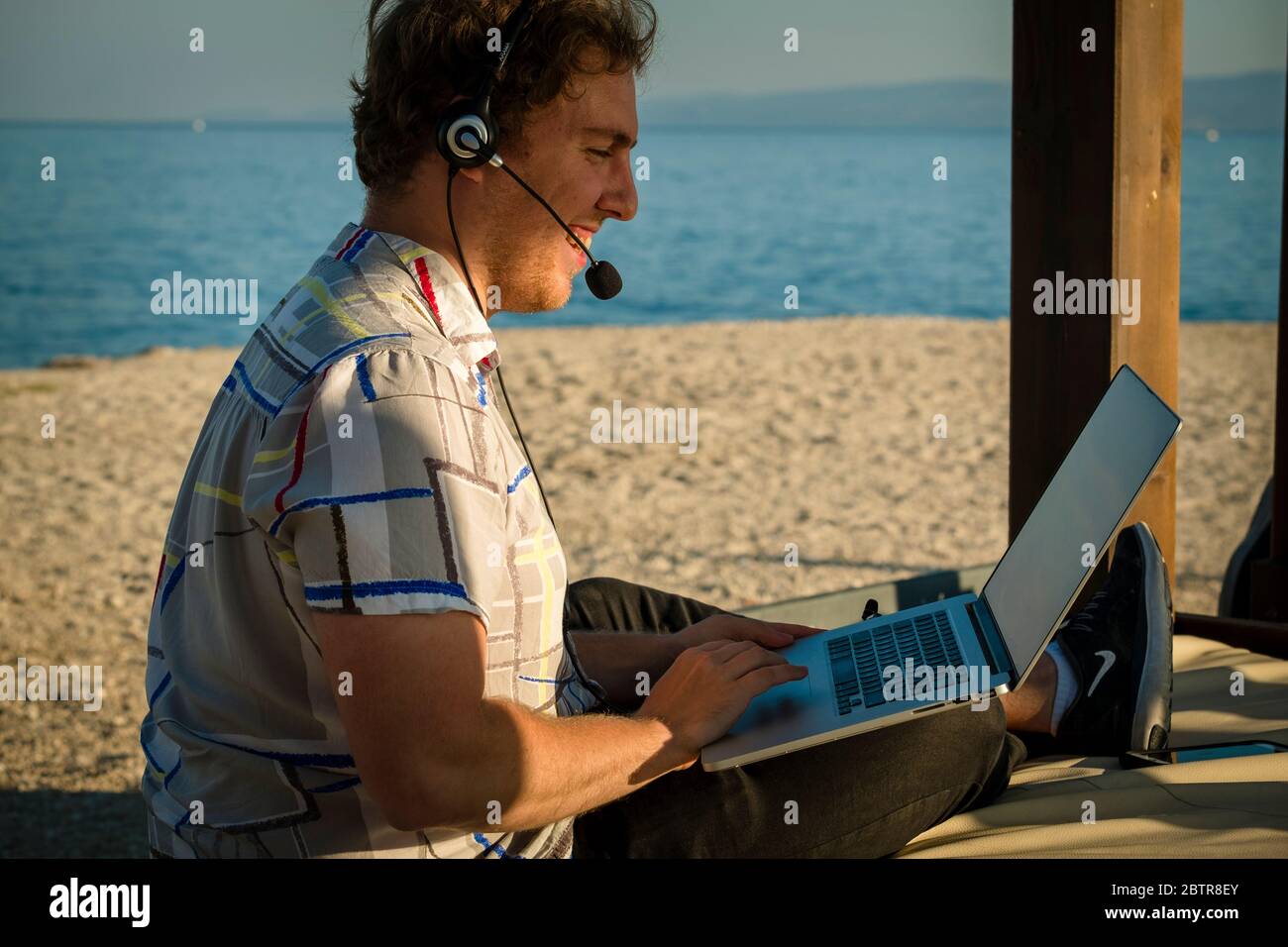 Un uomo che usa il laptop e le cuffie all'aperto in spiaggia Foto Stock