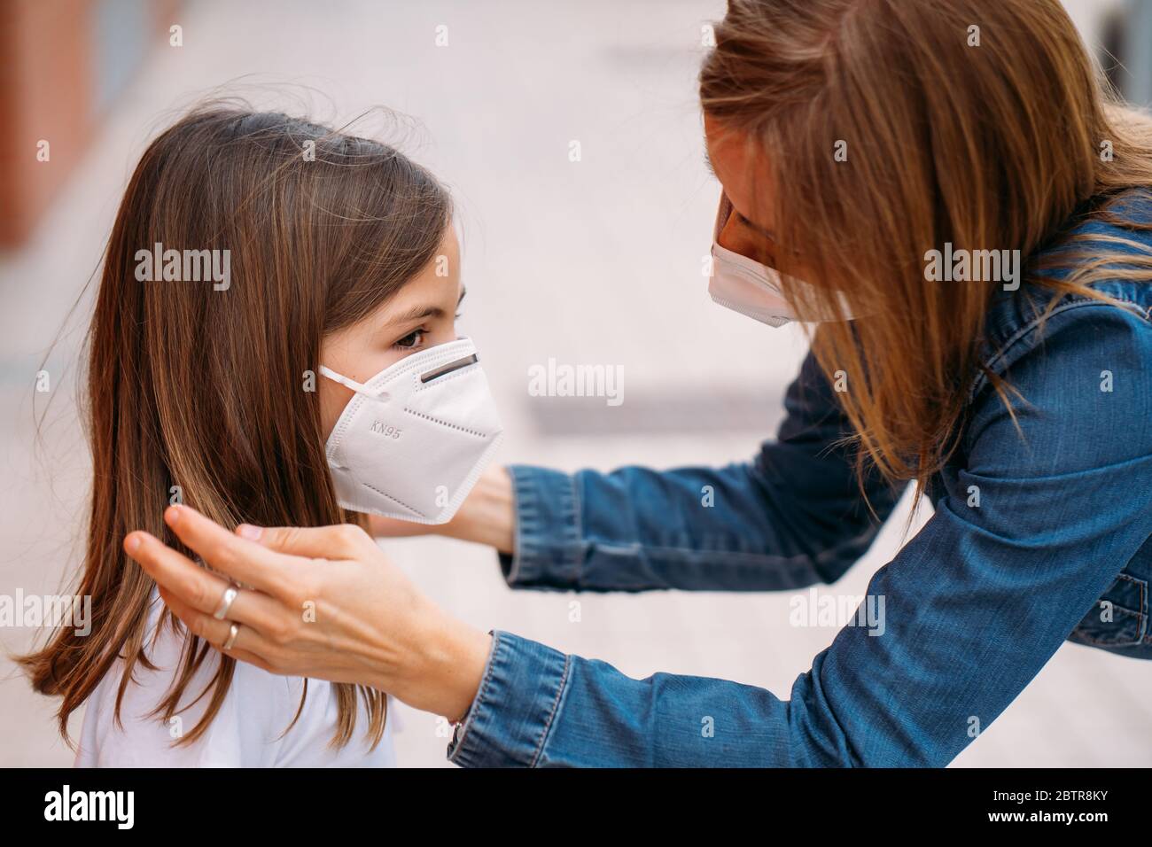 Madre che mette la maschera di faccia sulla sua figlia piccola sulla strada Foto Stock