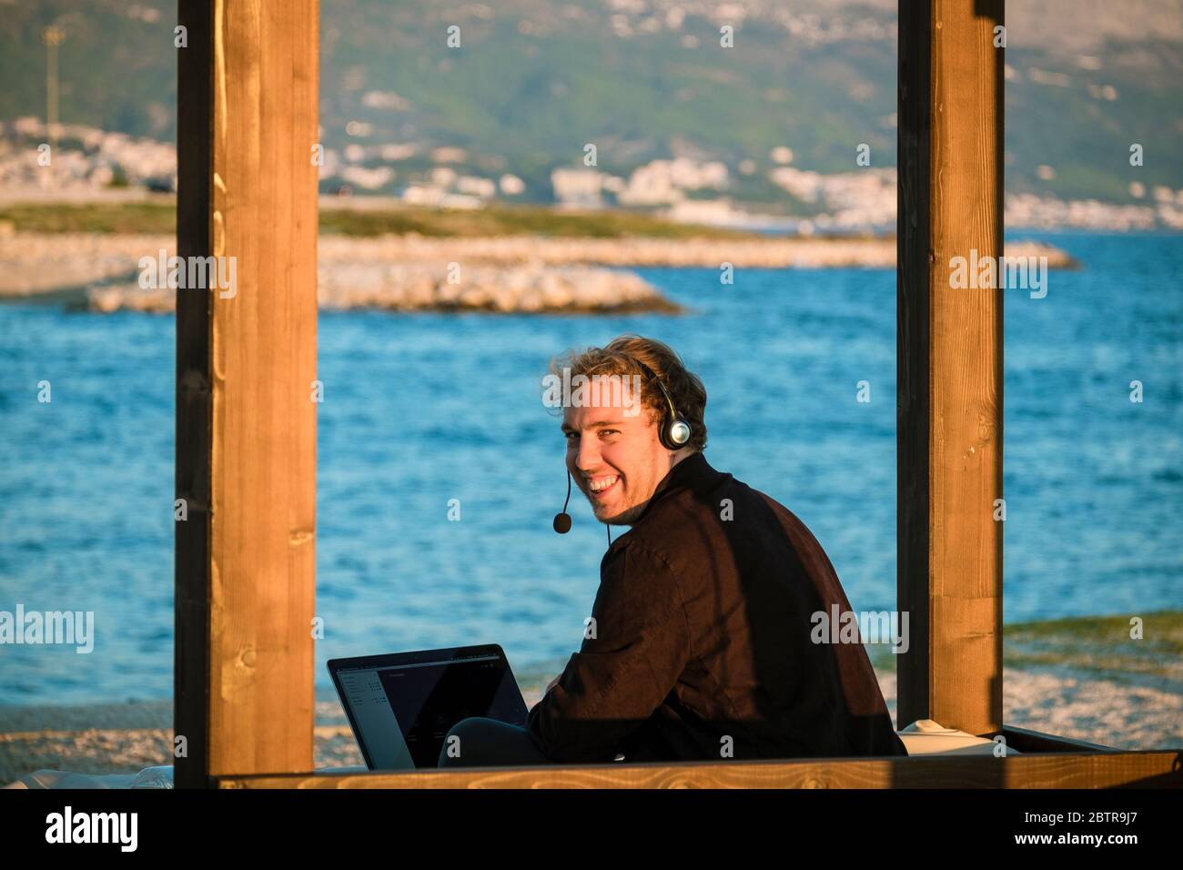 Un uomo che usa il laptop e le cuffie all'aperto in spiaggia Foto Stock