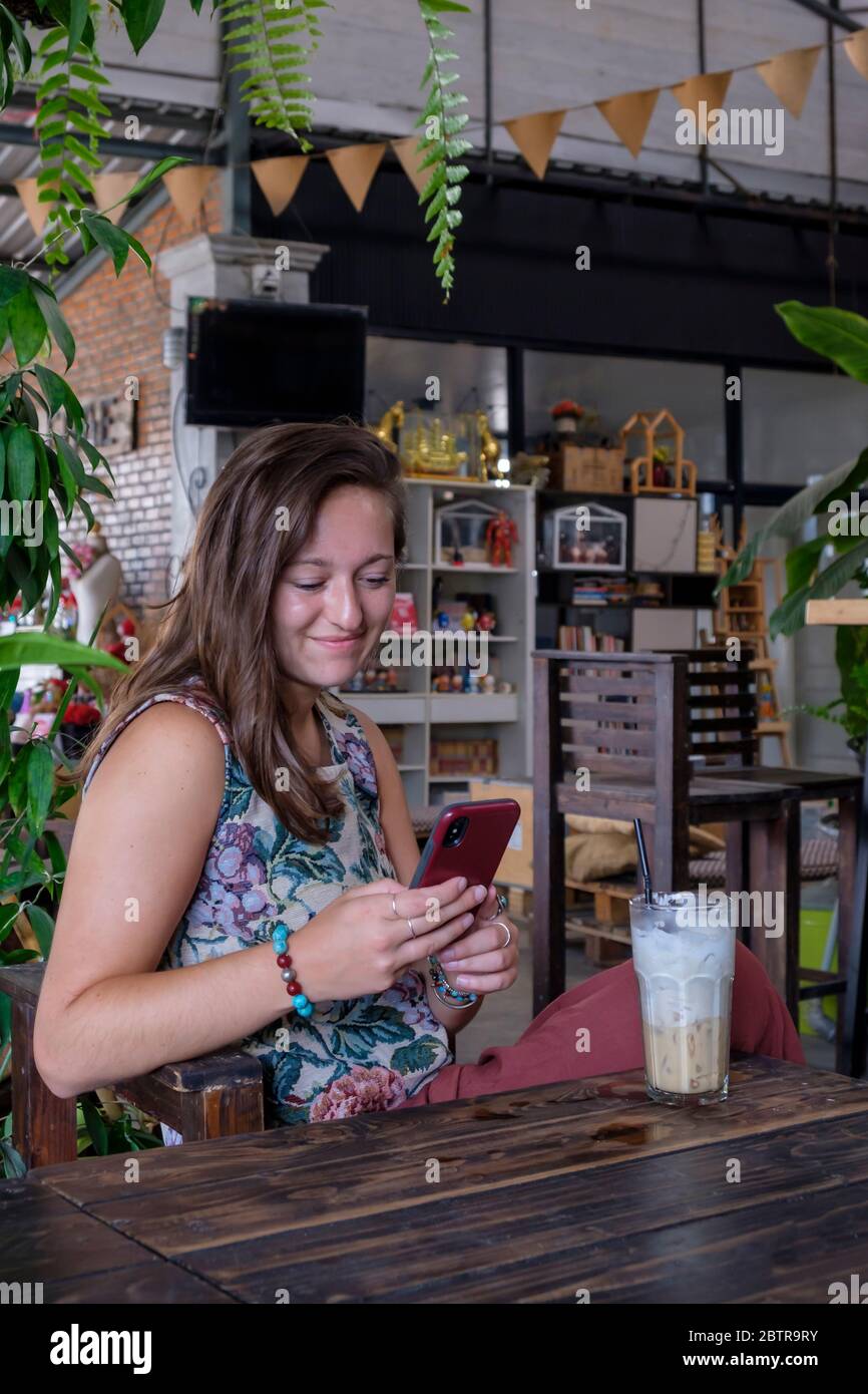 Giovane donna guarda il suo telefono cellulare con bevande ghiacciate sul tavolo in un bar Foto Stock
