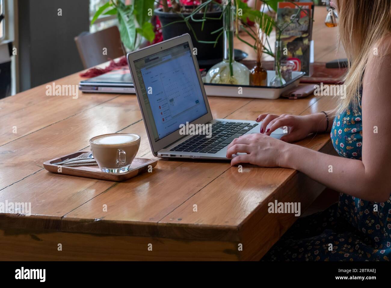 Una donna che lavora su un computer portatile, con una tazza di caffè in un ufficio domestico o in un caffè Foto Stock