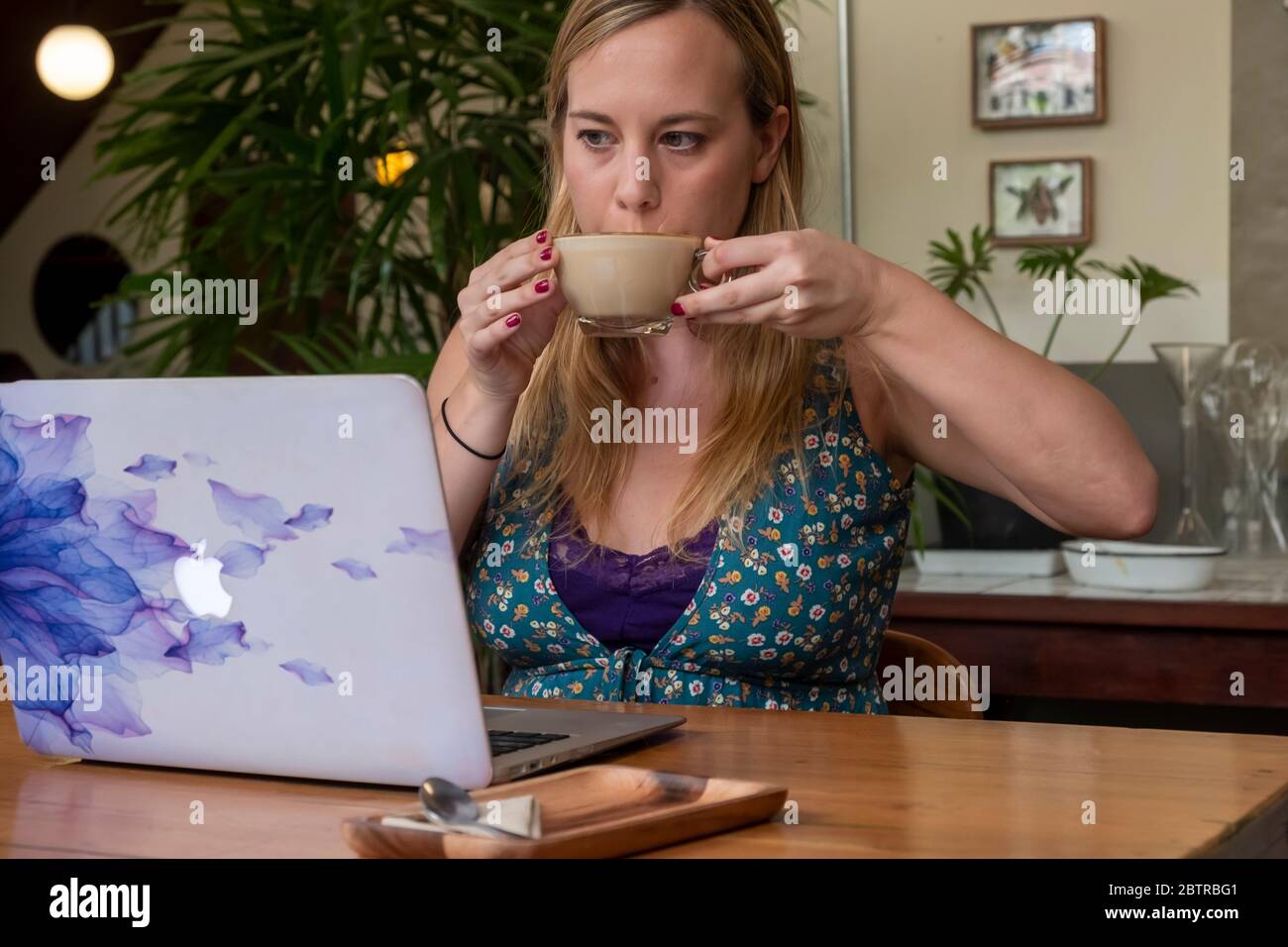 Una donna che lavora su un computer portatile, con una tazza di caffè in un ufficio domestico o in un caffè Foto Stock